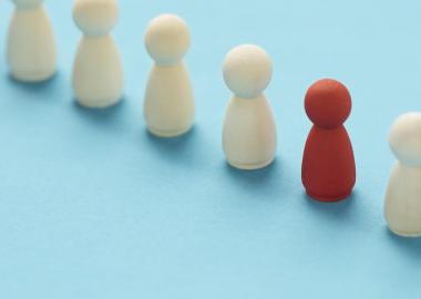 One red pawn in a line of brown wooden pawns on light blue surface